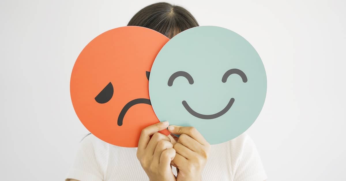 Woman holding sad face hiding behind happy face to symbolise bipolar depression | TPD Compensation Lawyers